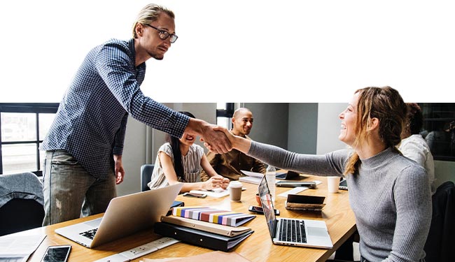 A man and a woman shake hands over a busy workspace