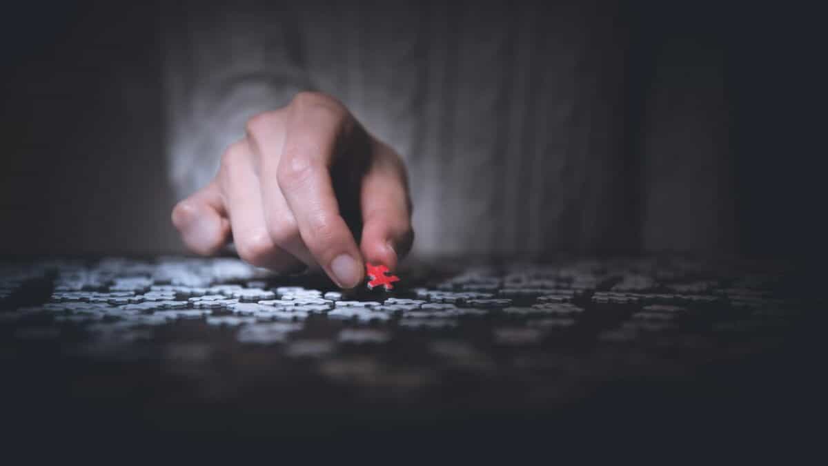 Man pulling a red puzzle piece from a pile of while puzzle pieces