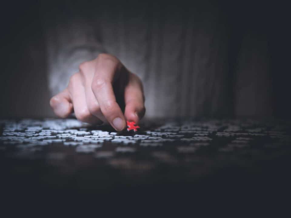 Man pulling a red puzzle piece from a pile of while puzzle pieces